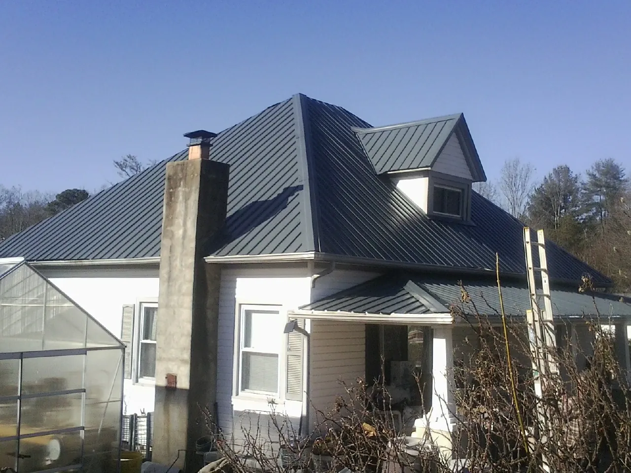 Dark blue standing seam metal roof on a white farmhouse with dormer — Slate & Tile Roof Repair by Roofing Brothers in Cuero