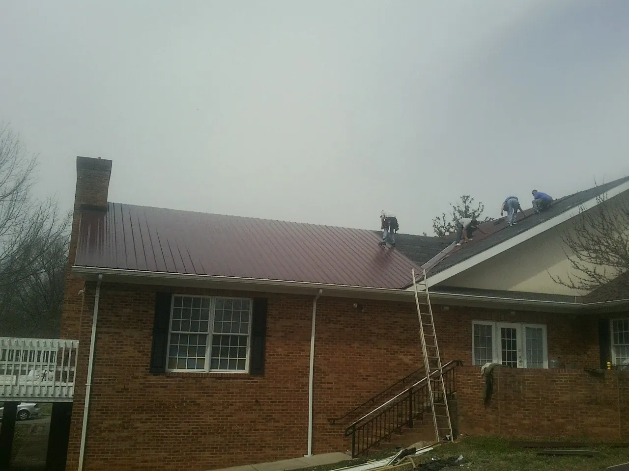 Crew setting red metal roofing panels on a brick home in Cuero