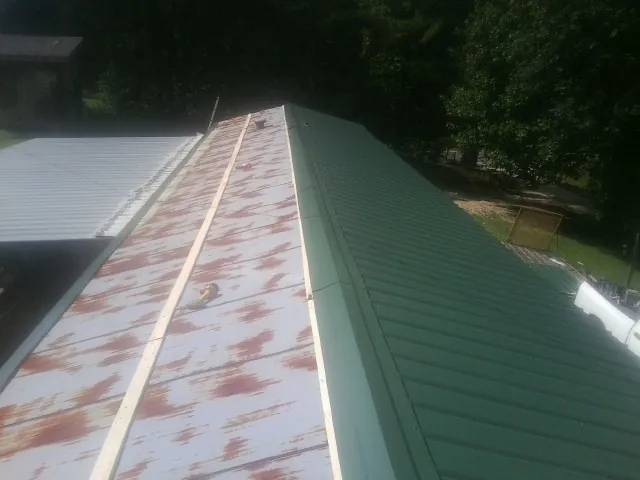 Old rusted panels beside newly installed green metal roofing — Wind Damage Roof Repair by Roofing Brothers in Cuero