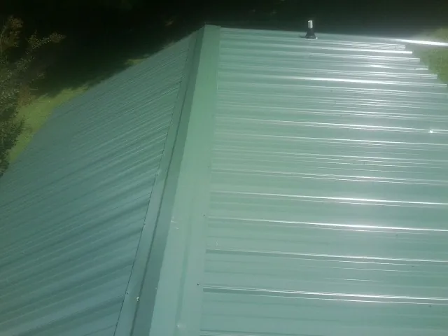 New green metal panels meeting at the ridge of a roof — Flat Roof Repair work by our crew in Cuero