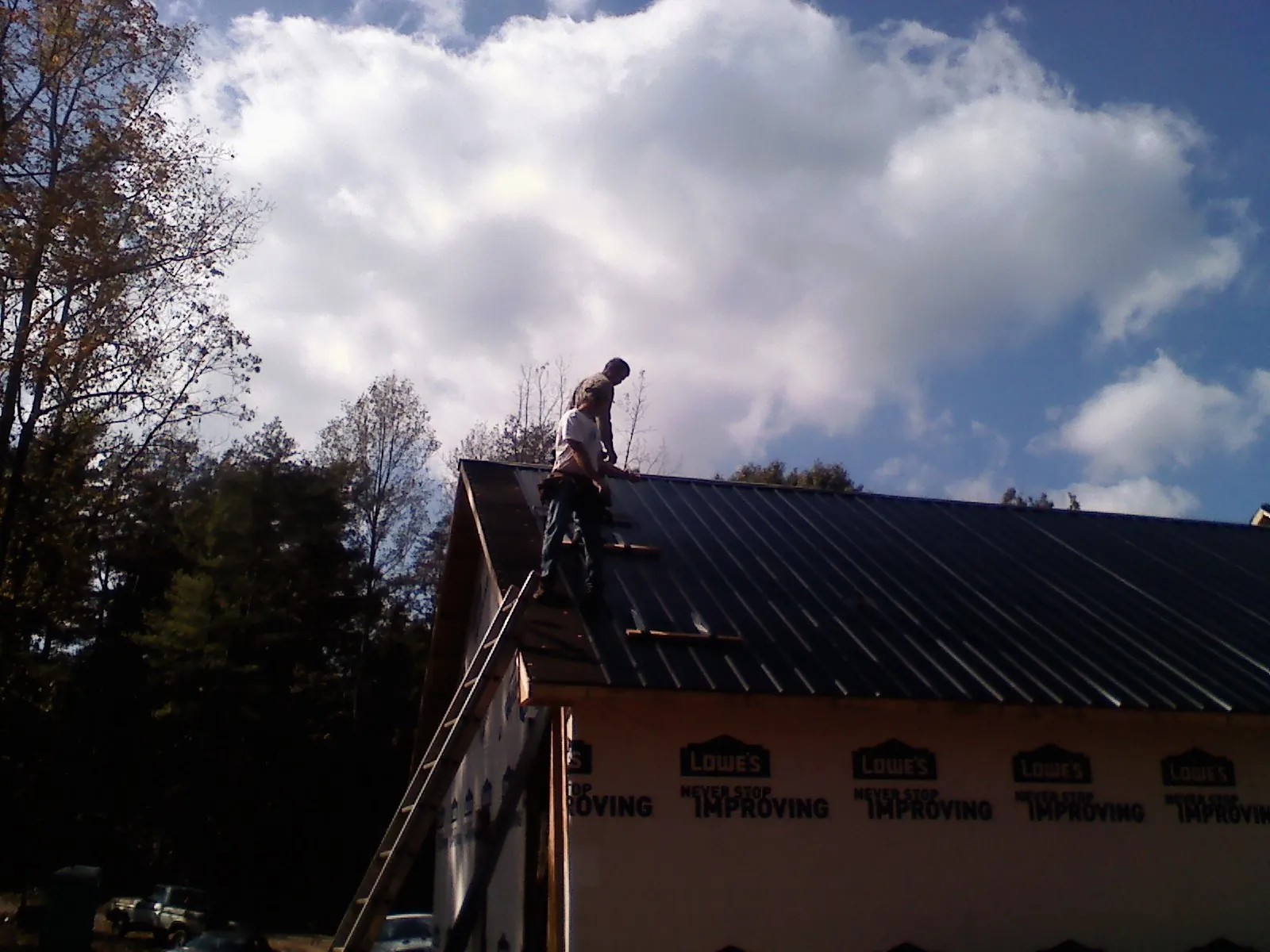 Roofer fastening dark metal panels high against a cloudy sky, from a Roof Inspection job in Cuero