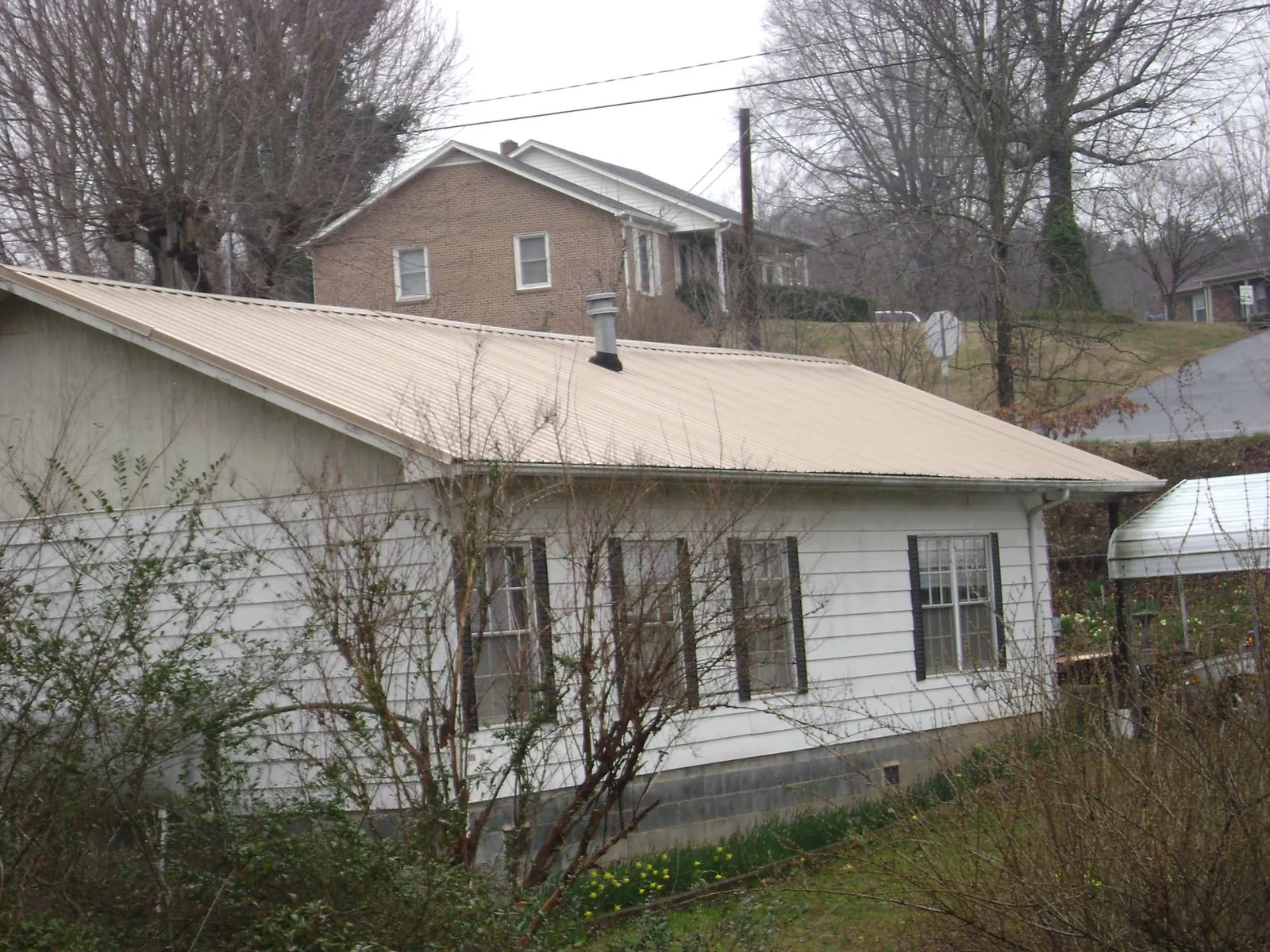 Tan metal roof on a white sided house set into a hillside — Commercial Roofing by Roofing Brothers in Cuero