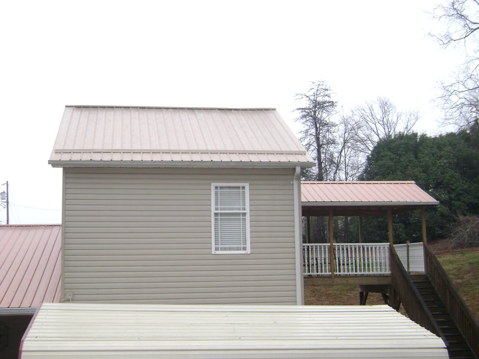 Tan metal roofs on a two story addition and attached porch, from a Roof Replacement job in Cuero