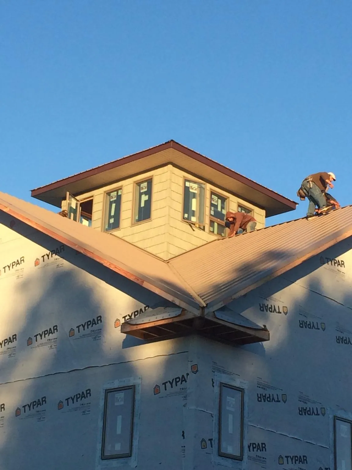 Roofers working around a rooftop cupola on a new metal roof at sunset — Roof Waterproofing in Cuero by Roofing Brothers